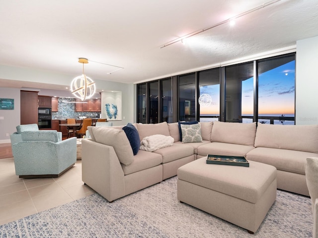 tiled living room featuring a chandelier, track lighting, and a wall of windows