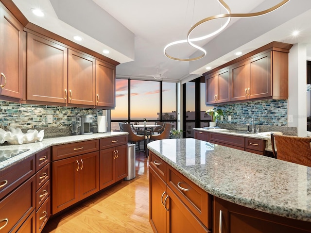 kitchen featuring hanging light fixtures, sink, light stone counters, and light wood-type flooring