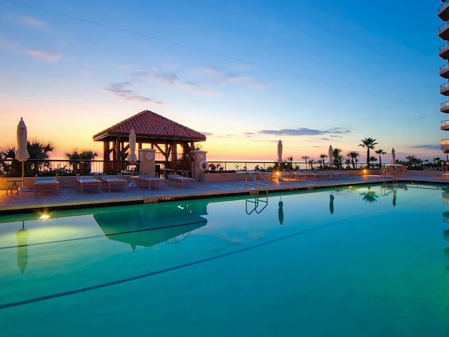 pool at dusk featuring a gazebo and a patio