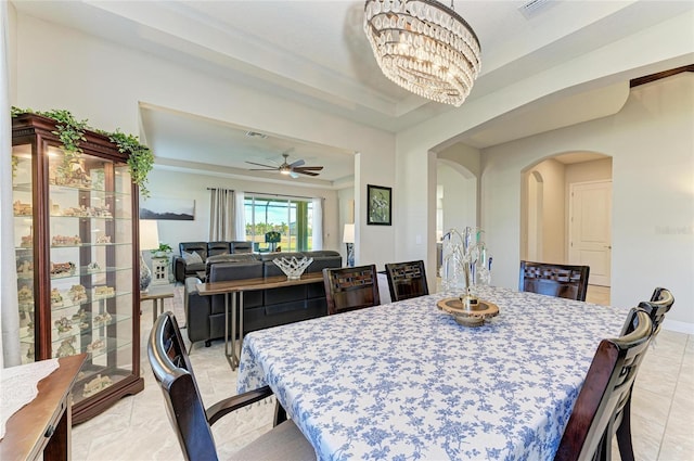 dining area with ceiling fan with notable chandelier and a raised ceiling