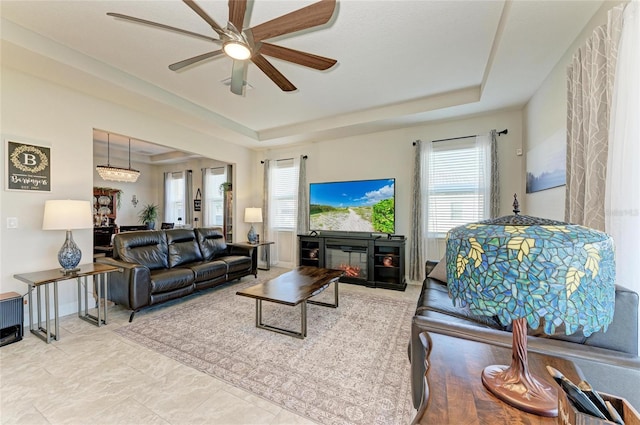 living room with a wealth of natural light, a raised ceiling, and ceiling fan