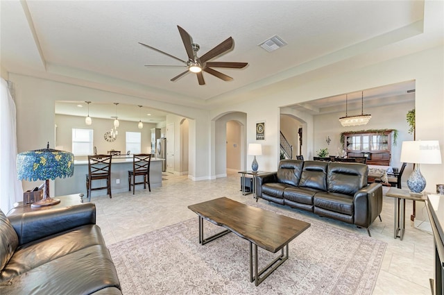 tiled living room with a tray ceiling and ceiling fan with notable chandelier