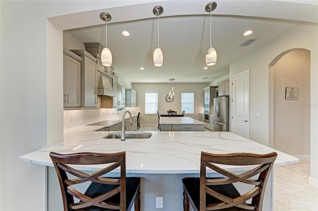 kitchen with premium range hood, a kitchen bar, sink, stainless steel fridge, and kitchen peninsula