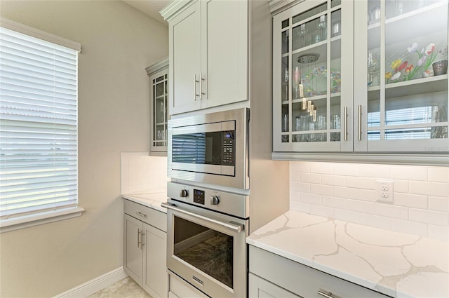 kitchen featuring light stone counters, stainless steel appliances, gray cabinets, and decorative backsplash