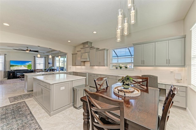 kitchen featuring decorative light fixtures, gray cabinets, kitchen peninsula, a kitchen island, and backsplash