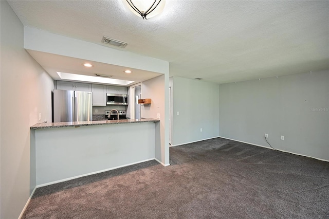 kitchen featuring appliances with stainless steel finishes, dark colored carpet, light stone counters, a textured ceiling, and kitchen peninsula