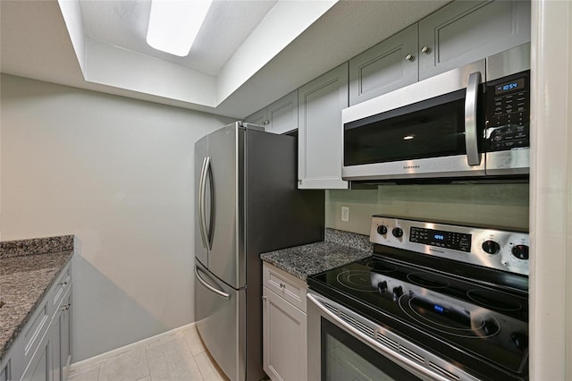 kitchen with stainless steel appliances, light tile patterned flooring, and dark stone countertops