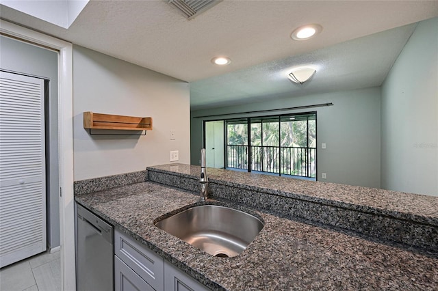 kitchen featuring light tile patterned flooring, sink, dark stone counters, stainless steel dishwasher, and a textured ceiling