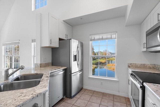 kitchen with light tile patterned flooring, sink, appliances with stainless steel finishes, light stone countertops, and white cabinets