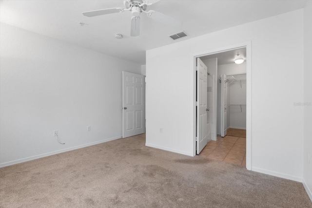 unfurnished bedroom featuring a walk in closet, light colored carpet, ceiling fan, and a closet