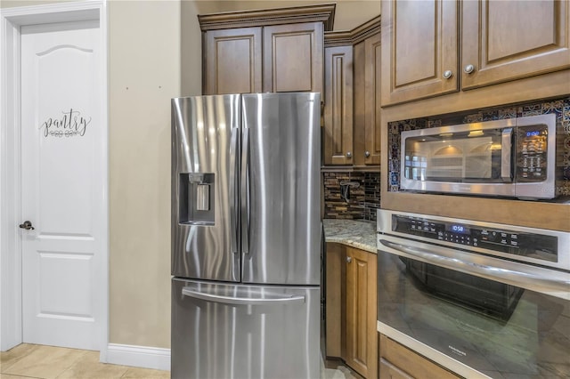 kitchen with light stone counters, stainless steel appliances, light tile patterned flooring, and backsplash