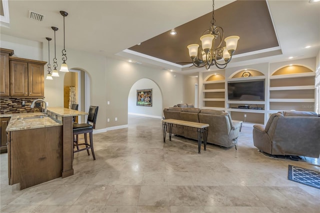 living room with a raised ceiling, sink, a chandelier, and built in shelves