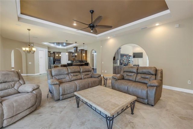 living room featuring a raised ceiling and ceiling fan with notable chandelier