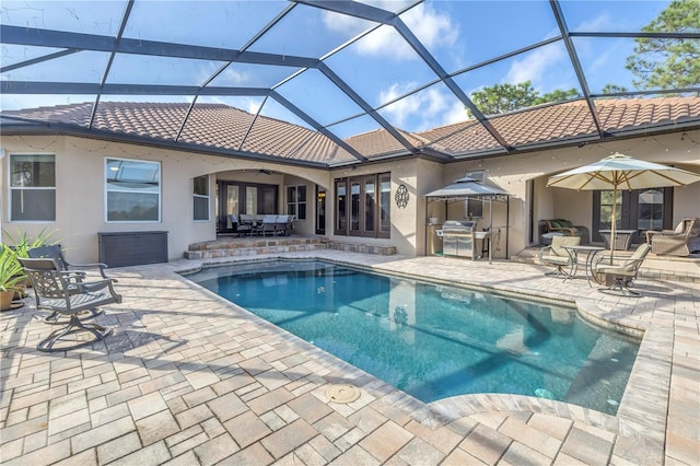 view of pool with an outdoor kitchen, a patio area, area for grilling, glass enclosure, and ceiling fan