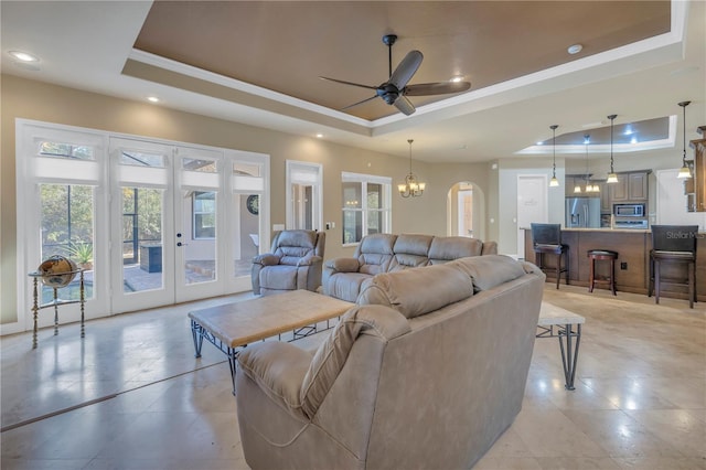 living room with a tray ceiling, ceiling fan with notable chandelier, and french doors