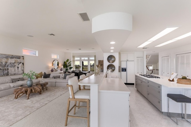 kitchen with sink, white cabinetry, a spacious island, paneled fridge, and a kitchen bar