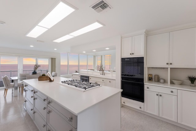 kitchen with white cabinetry, a water view, a center island, light tile patterned floors, and black appliances