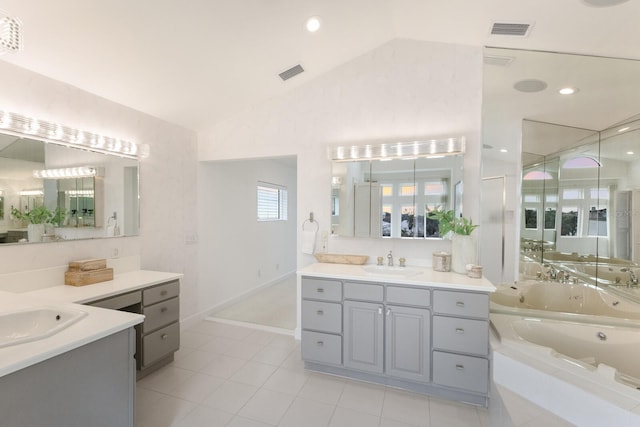 bathroom with tile patterned floors, vanity, tiled bath, and vaulted ceiling