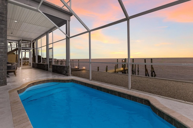 pool at dusk featuring a lanai, a patio area, and a water view