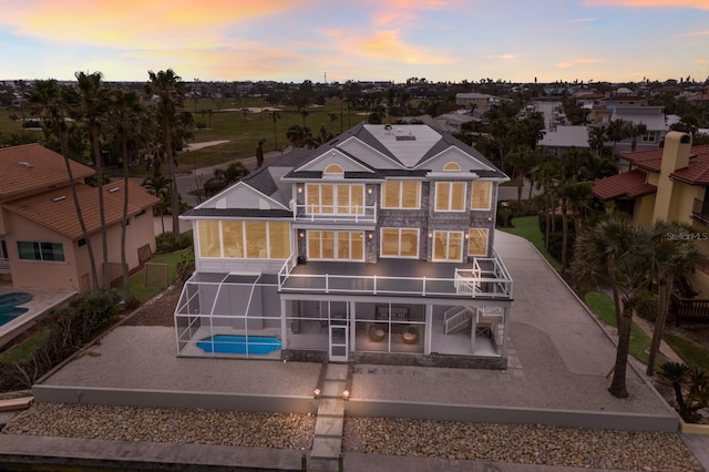 back house at dusk featuring glass enclosure, a fenced in pool, and a patio area