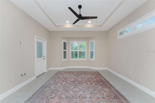 empty room featuring a raised ceiling, ornamental molding, a healthy amount of sunlight, and ceiling fan