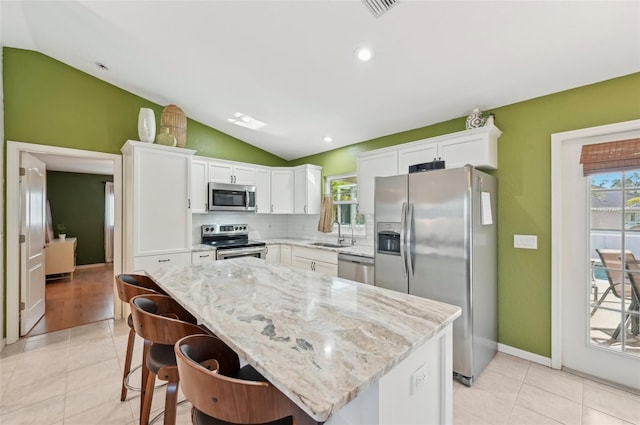 kitchen featuring lofted ceiling, sink, white cabinetry, stainless steel appliances, and a kitchen island