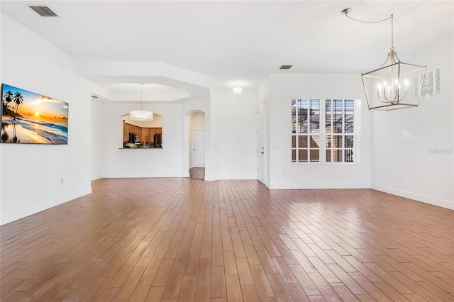 unfurnished living room with wood-type flooring, a tray ceiling, and a chandelier