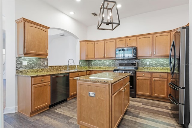 kitchen with sink, appliances with stainless steel finishes, a center island, light stone counters, and decorative light fixtures