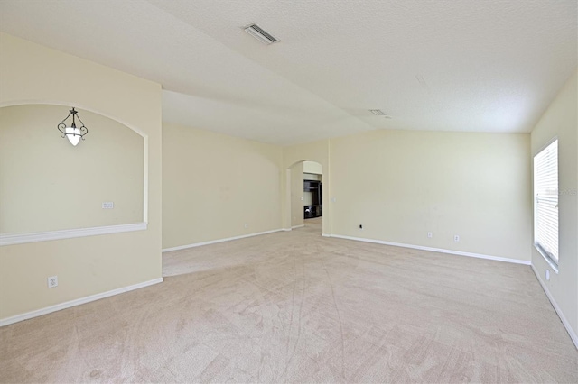 carpeted empty room featuring vaulted ceiling and a textured ceiling