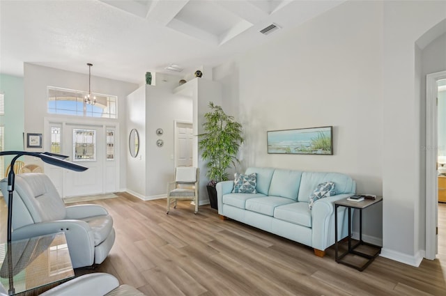 living room featuring beam ceiling, coffered ceiling, hardwood / wood-style floors, and an inviting chandelier