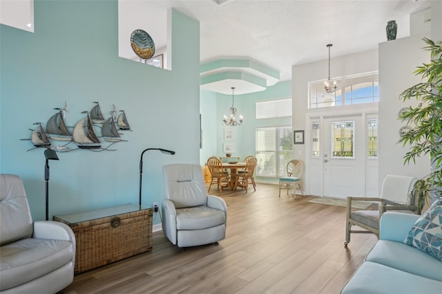 living room with light wood-type flooring, an inviting chandelier, and a towering ceiling