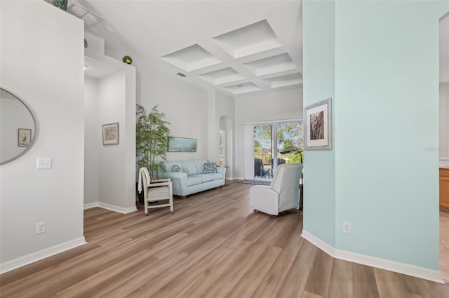 unfurnished living room featuring coffered ceiling, light hardwood / wood-style floors, beamed ceiling, and a high ceiling