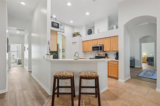 kitchen featuring stainless steel appliances, a high ceiling, a kitchen bar, light brown cabinetry, and kitchen peninsula