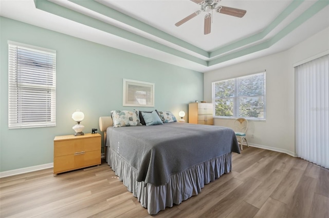 bedroom featuring ceiling fan, a raised ceiling, and light wood-type flooring