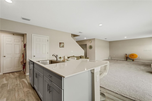 kitchen with a kitchen bar, sink, stainless steel dishwasher, gray cabinets, and an island with sink