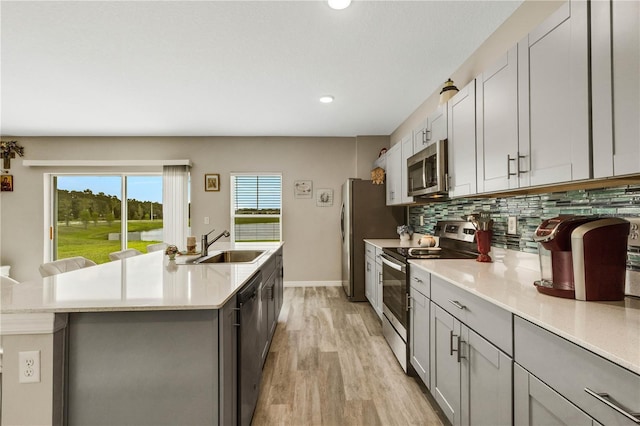 kitchen featuring sink, light hardwood / wood-style flooring, a kitchen island with sink, stainless steel appliances, and tasteful backsplash