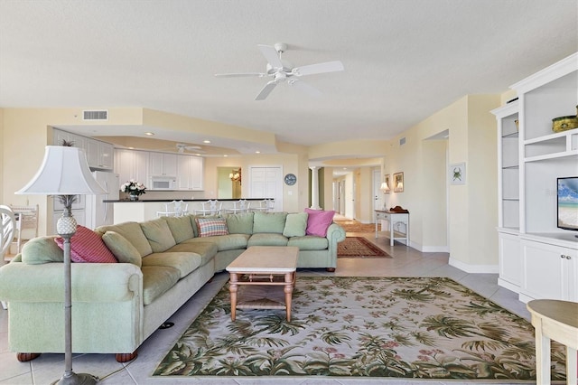 living room with a textured ceiling, ceiling fan, and light tile patterned flooring