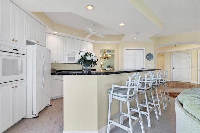 kitchen with light tile patterned floors, white appliances, a breakfast bar, white cabinetry, and a kitchen island