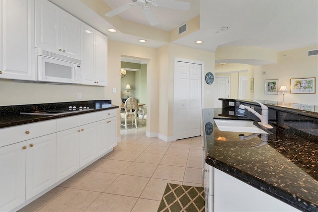 kitchen with sink, stovetop, white cabinets, light tile patterned flooring, and dark stone counters