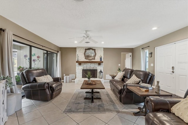 tiled living room featuring ceiling fan, a stone fireplace, and a textured ceiling