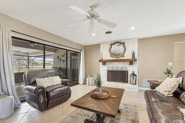 living room with light tile patterned floors, a stone fireplace, a textured ceiling, and ceiling fan