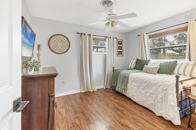 bedroom featuring ceiling fan, dark hardwood / wood-style flooring, multiple windows, and a textured ceiling