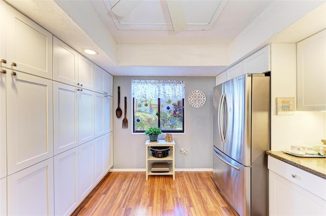 kitchen with stainless steel refrigerator, white cabinetry, dark stone counters, and light hardwood / wood-style flooring