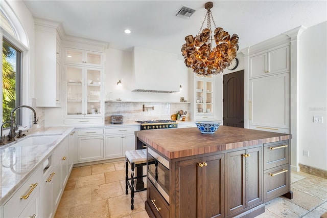 kitchen featuring a kitchen island, stainless steel microwave, wood counters, white cabinetry, and sink