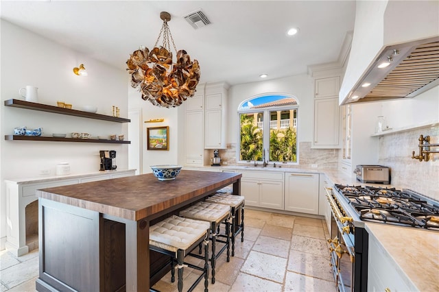 kitchen featuring premium range hood, a kitchen island, butcher block countertops, white cabinetry, and a breakfast bar area