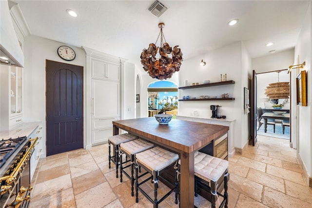 kitchen with wooden counters, custom range hood, gas stove, white cabinets, and a chandelier