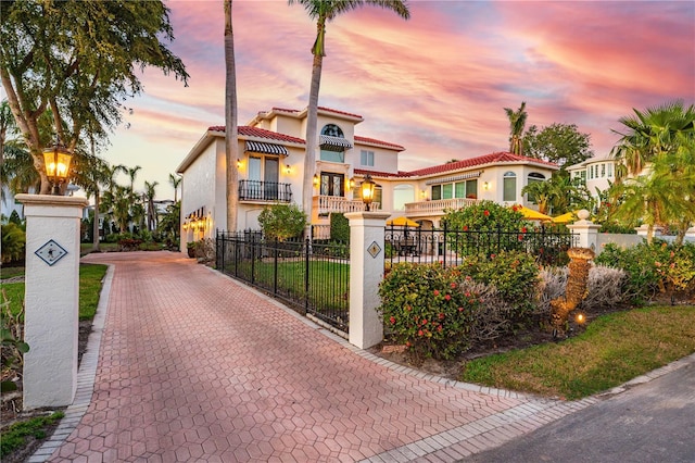 mediterranean / spanish house with a fenced front yard, a tile roof, a balcony, and stucco siding