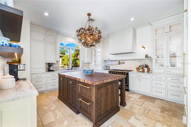 kitchen featuring butcher block counters, a kitchen island, white cabinetry, glass insert cabinets, and custom range hood