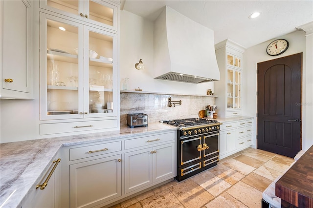 kitchen featuring white cabinets, premium range hood, light stone counters, and range with two ovens