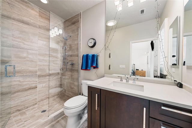 full bath with a tile shower, toilet, vanity, and visible vents